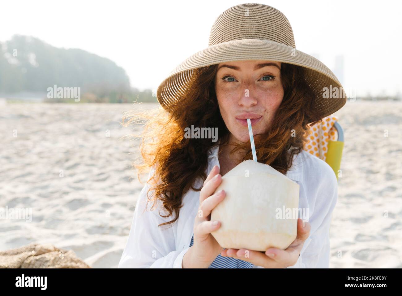 Femme buvant de l'eau de coco à la plage Banque D'Images