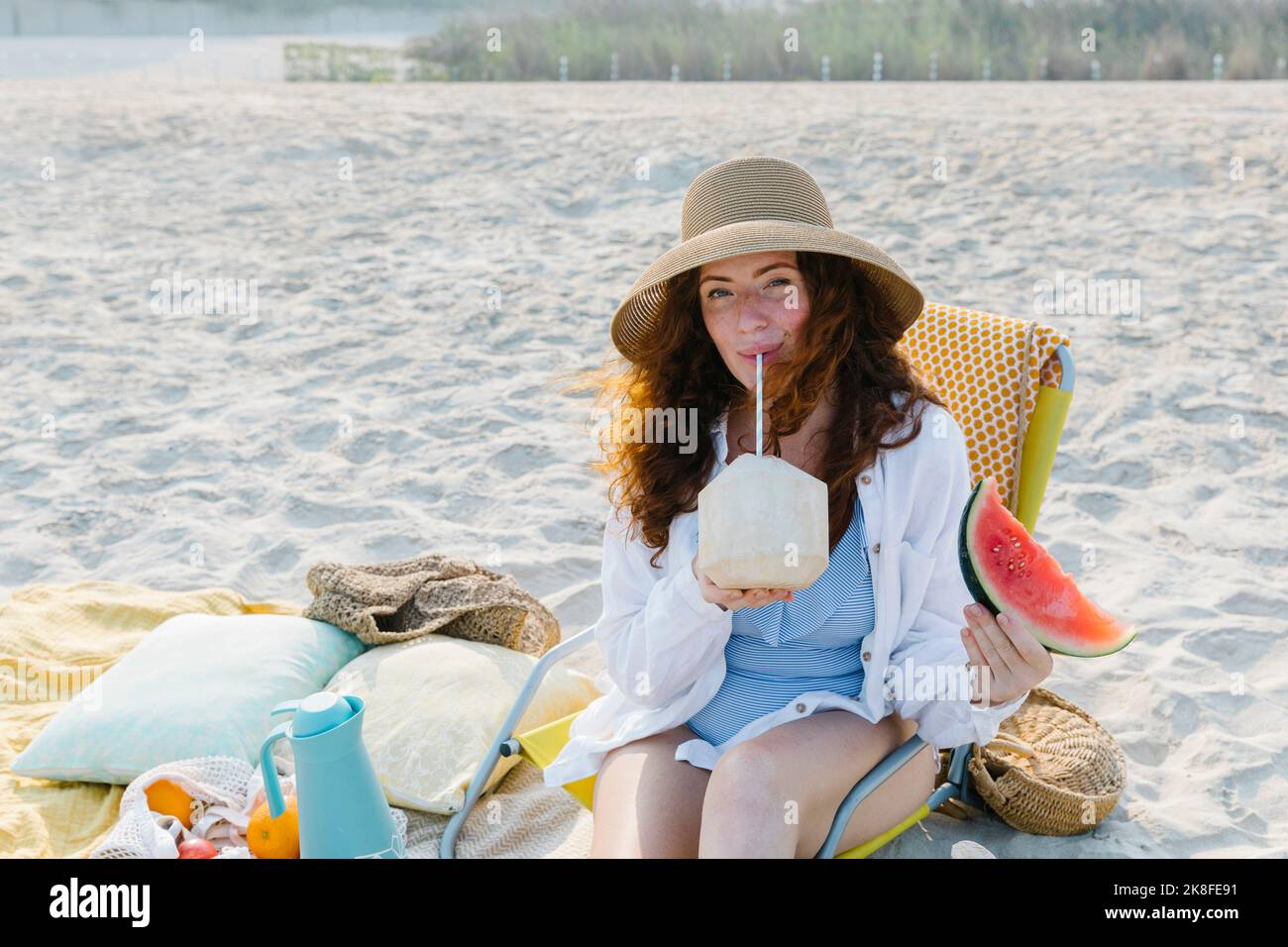 Femme portant un chapeau buvant de l'eau de coco à la plage Banque D'Images