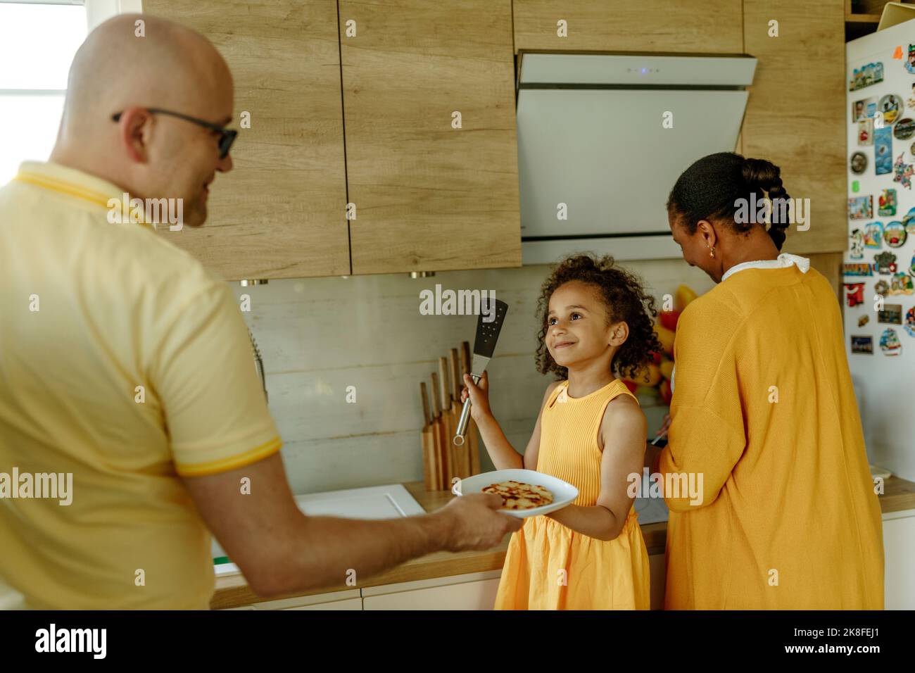 Fille souriante donnant une assiette au père debout par la mère dans la cuisine Banque D'Images