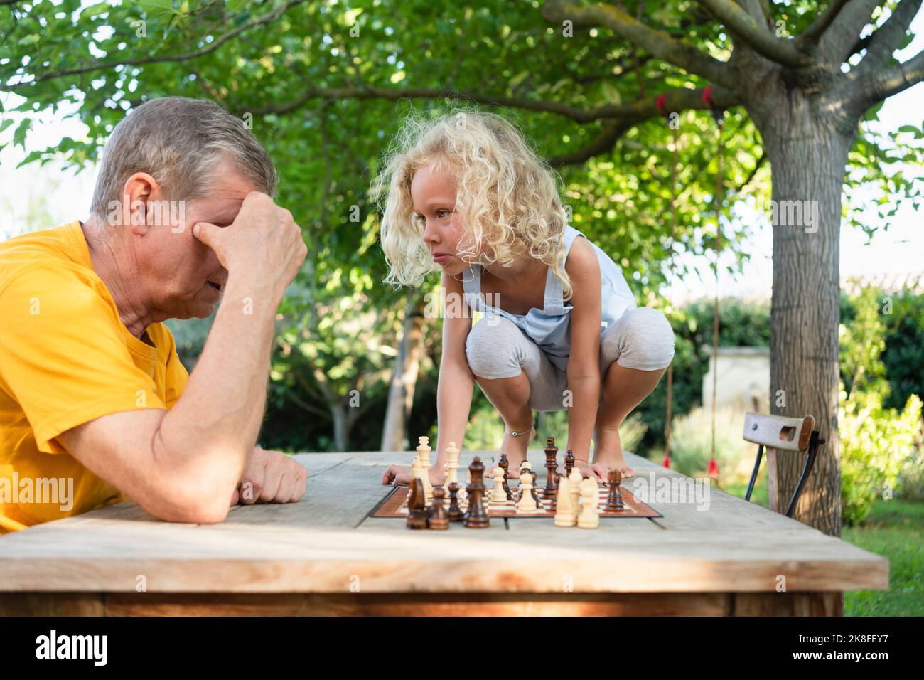 Grand-père jouant aux échecs avec la petite-fille assise sur une table Banque D'Images