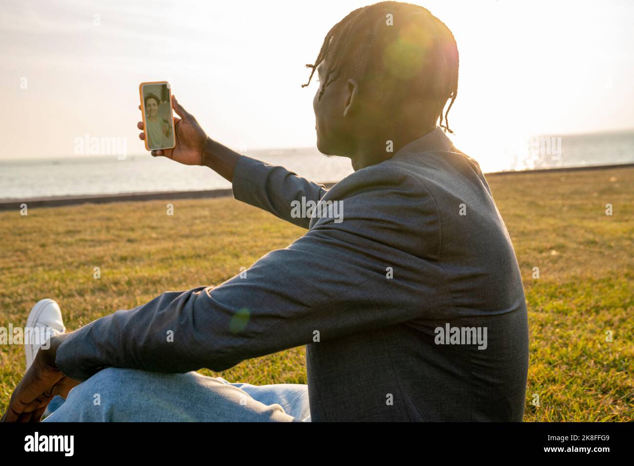 Homme d'affaires ayant des appels vidéo par smartphone assis sur l'herbe Banque D'Images