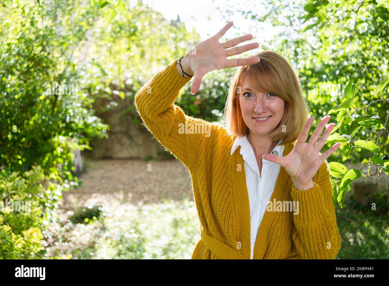 Femme mûre faisant le cadre de doigt à travers les mains dans le jardin Banque D'Images