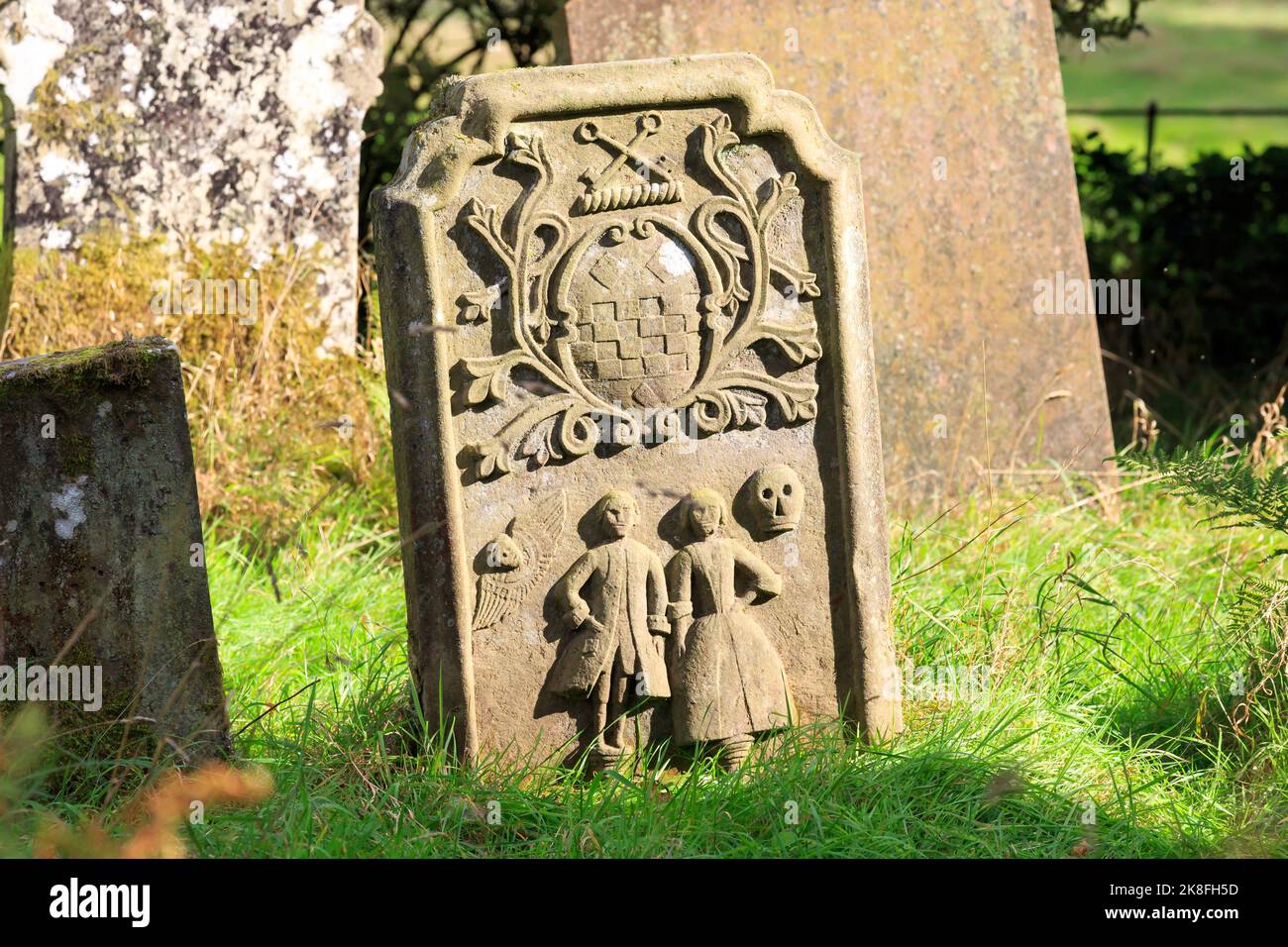 Une pierre tombale médiévale avec des figures sculptées dans un vieux cimetière éclairé par le soleil du soir Banque D'Images