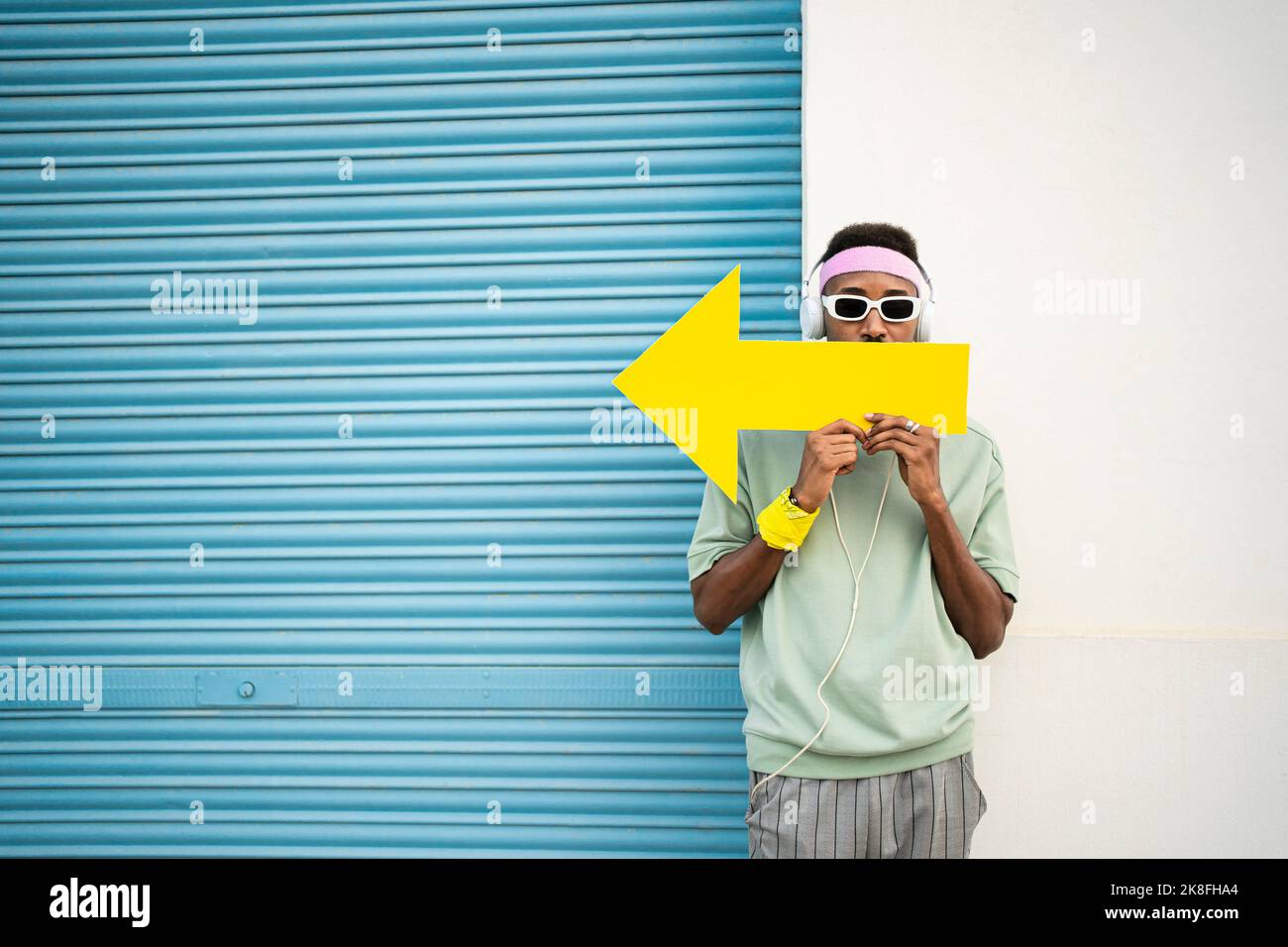 Homme tenant le signe de la flèche jaune devant les lèvres par un obturateur bleu Banque D'Images