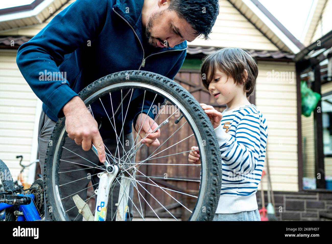 Garçon regardant le père répare la roue de vélo à l'extérieur de la maison Banque D'Images