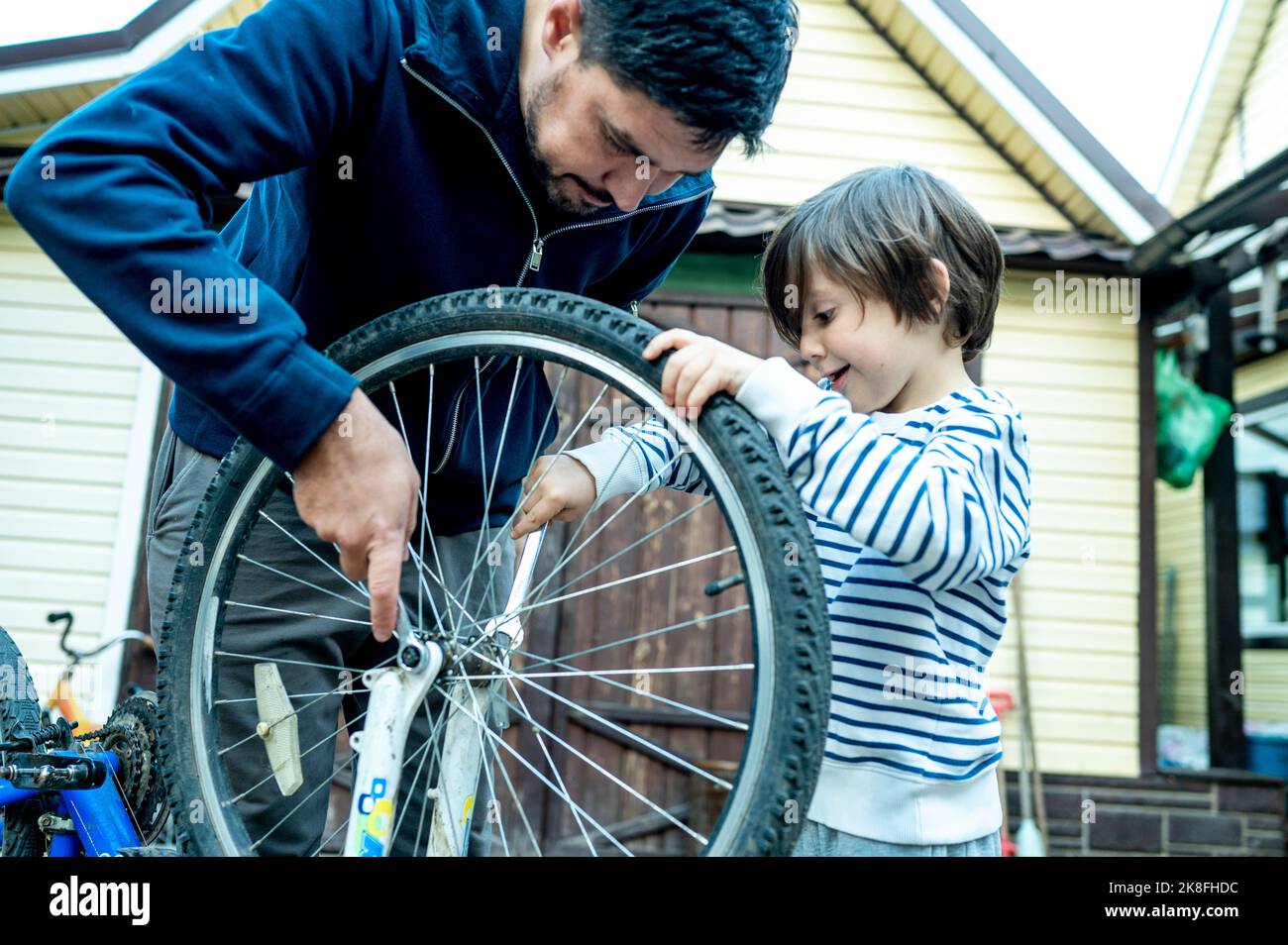 Fils aidant le père à réparer la roue de vélo à l'extérieur de la maison Banque D'Images