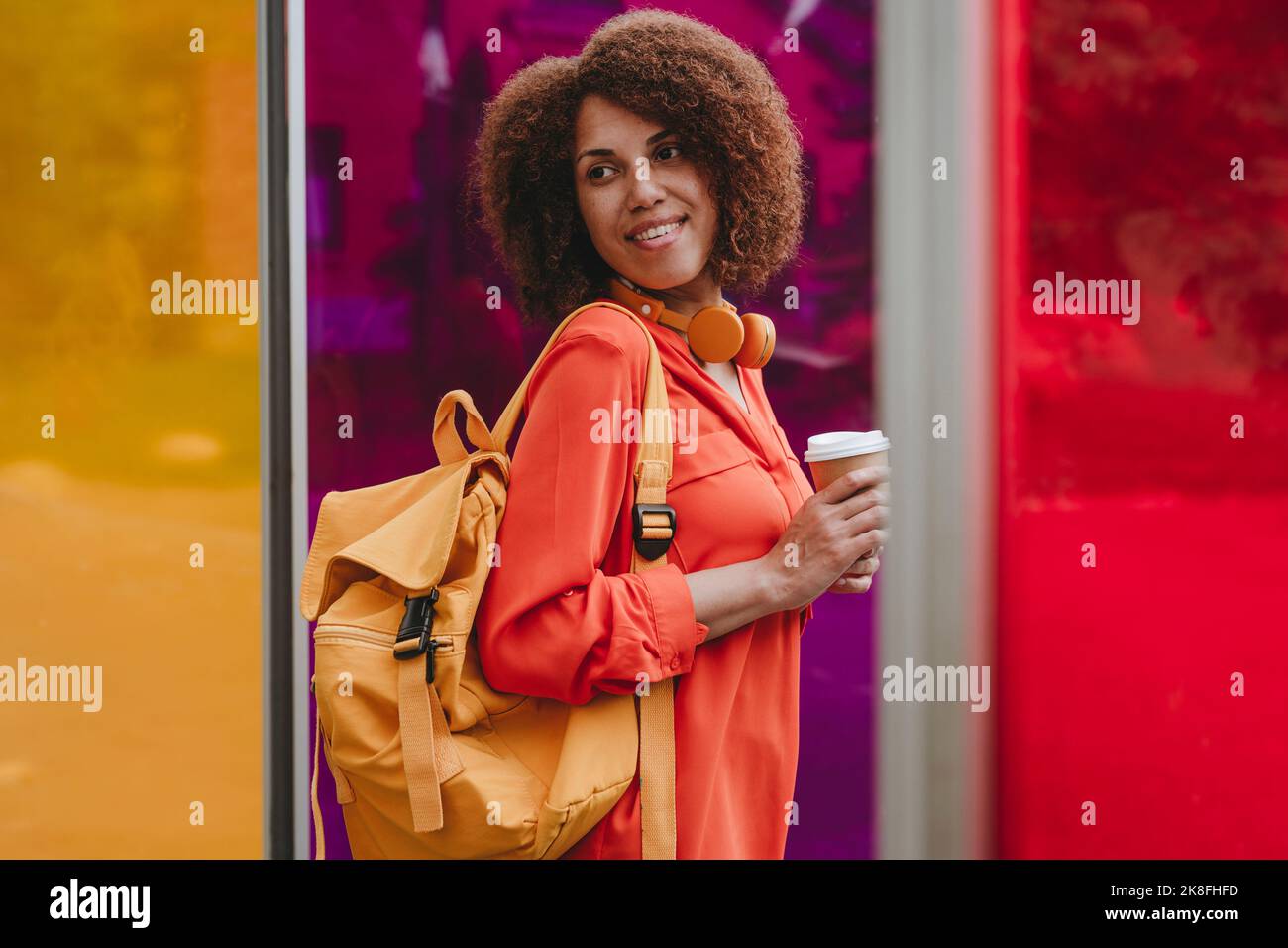 Femme souriante avec sac à dos et tasse à café jetable par des verres de couleur vibrante Banque D'Images