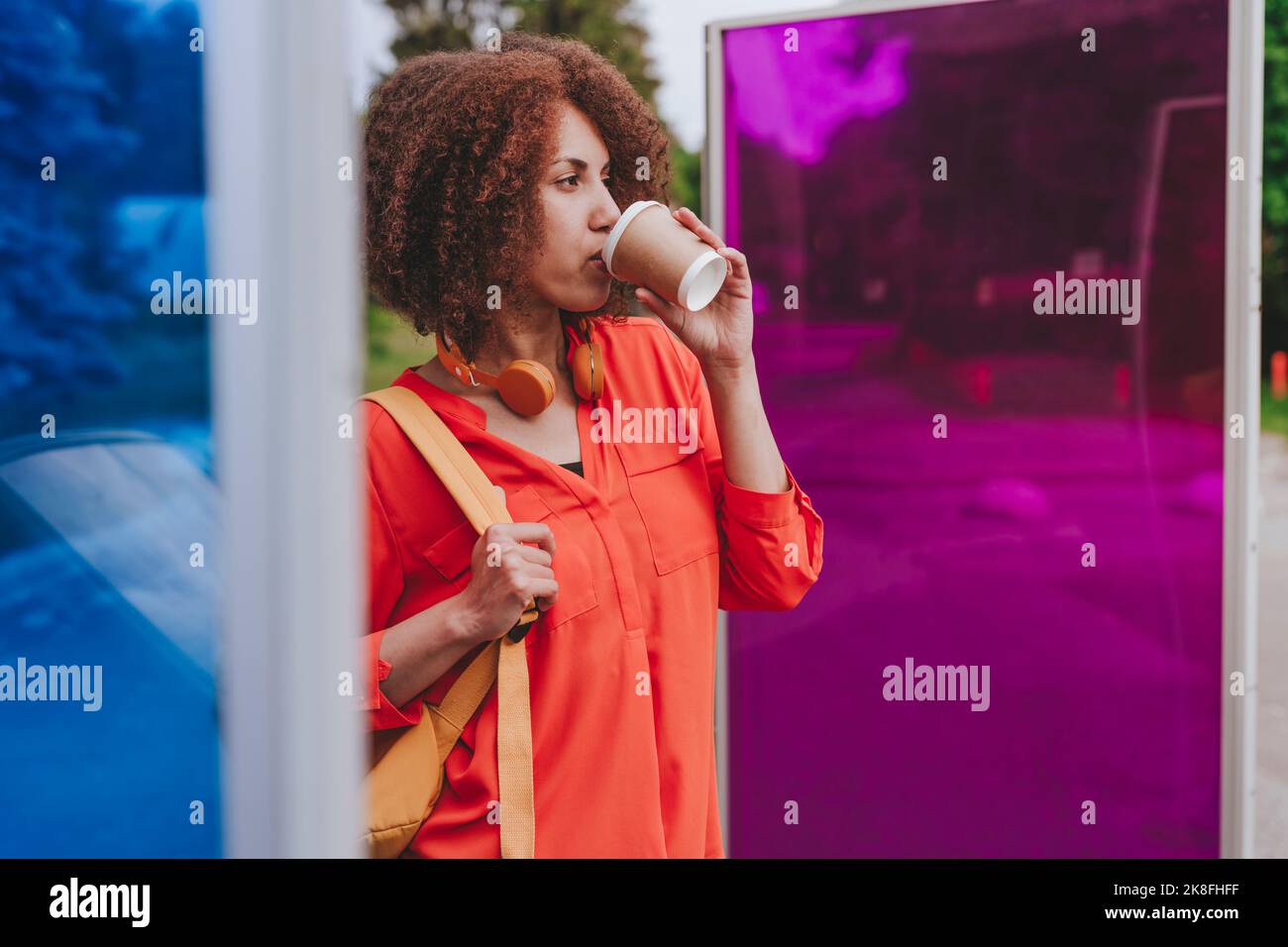 Une jeune femme boit du café près des verres magenta et bleu Banque D'Images