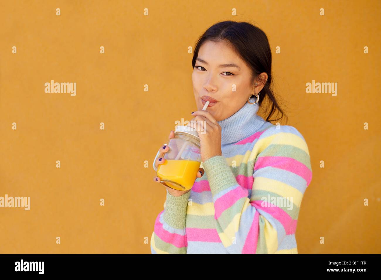 Femme buvant du jus d'orange devant le mur jaune Banque D'Images