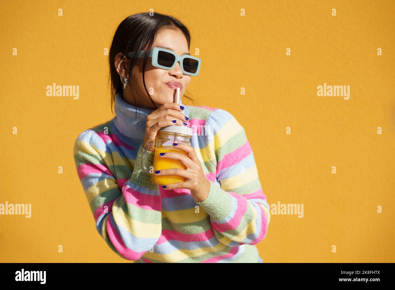 Jeune femme buvant du jus d'orange devant le mur jaune Banque D'Images