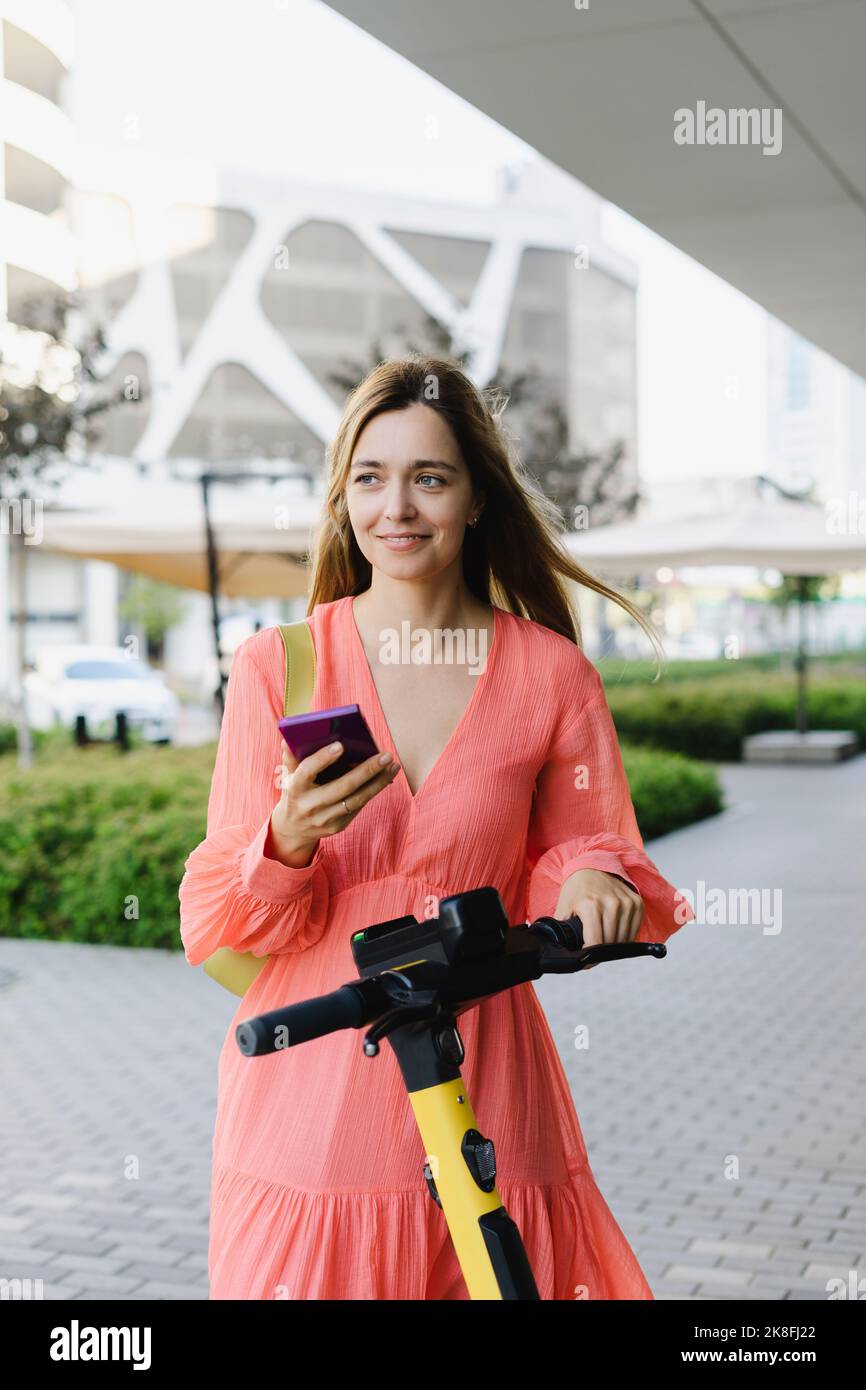 Femme souriante tenant un smartphone debout avec un scooter électrique sur la piste de marche Banque D'Images