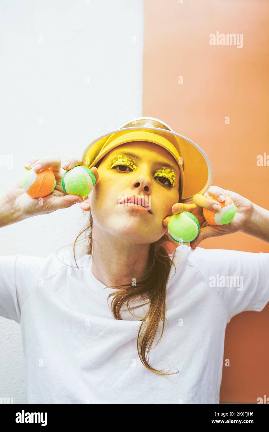 Sportswoman tenant des balles de tennis portant un pare-soleil sur fond coloré Banque D'Images