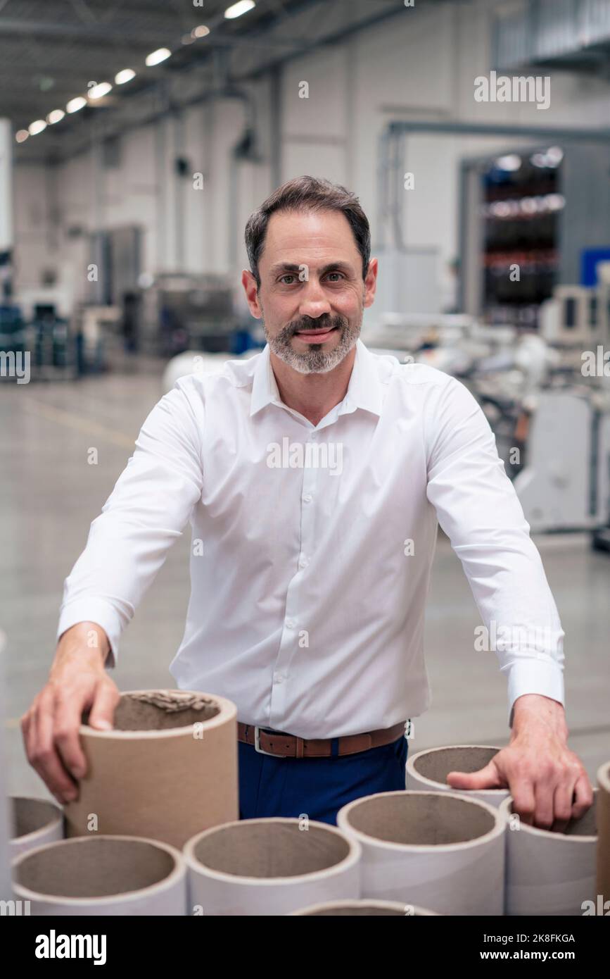 Homme d'affaires souriant devant des tubes en carton dans l'industrie Banque D'Images