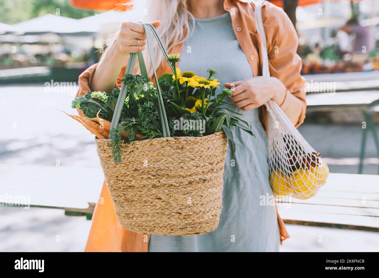 Femme tenant des fleurs et des légumes dans un sac en osier au marché local Banque D'Images
