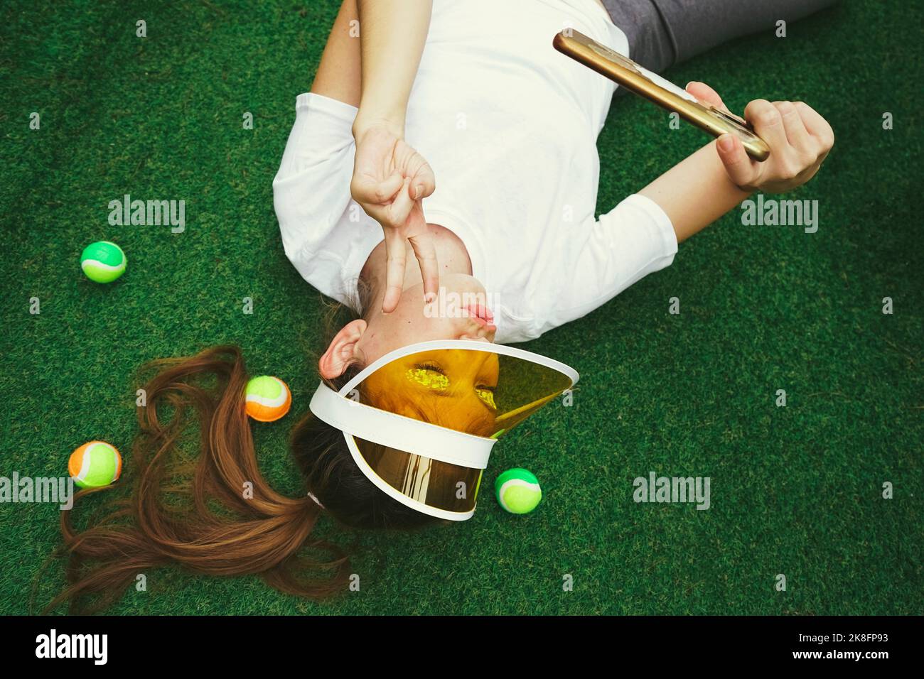 Femme portant un chapeau de pare-soleil faisant signe de paix et prenant le selfie à travers un smartphone sur un terrain de sport Banque D'Images