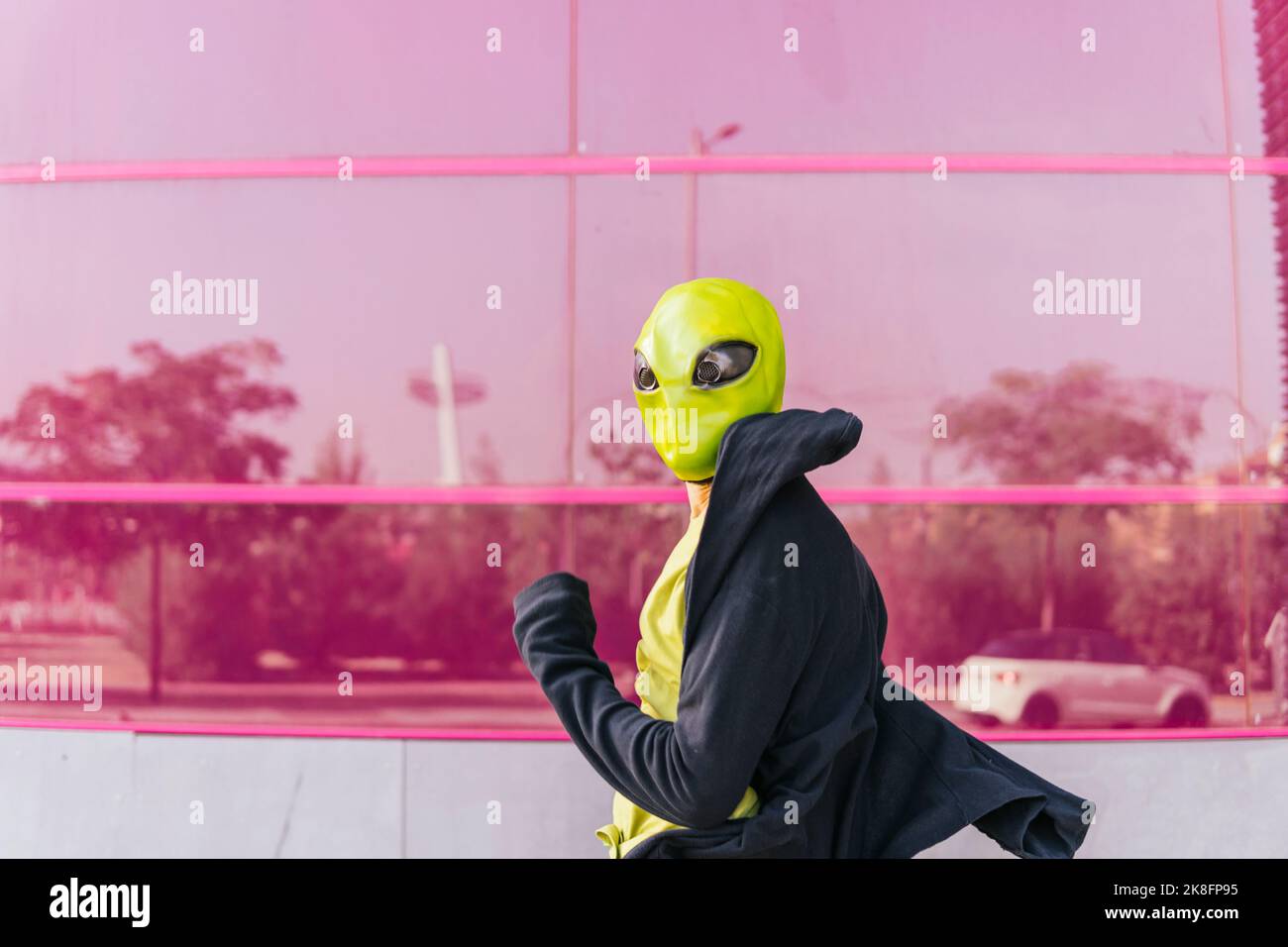Homme portant un masque extraterrestre devant un mur en verre rose Banque D'Images
