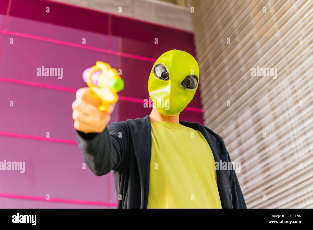 Homme portant un masque extraterrestre jouant avec un pistolet à jouets Banque D'Images