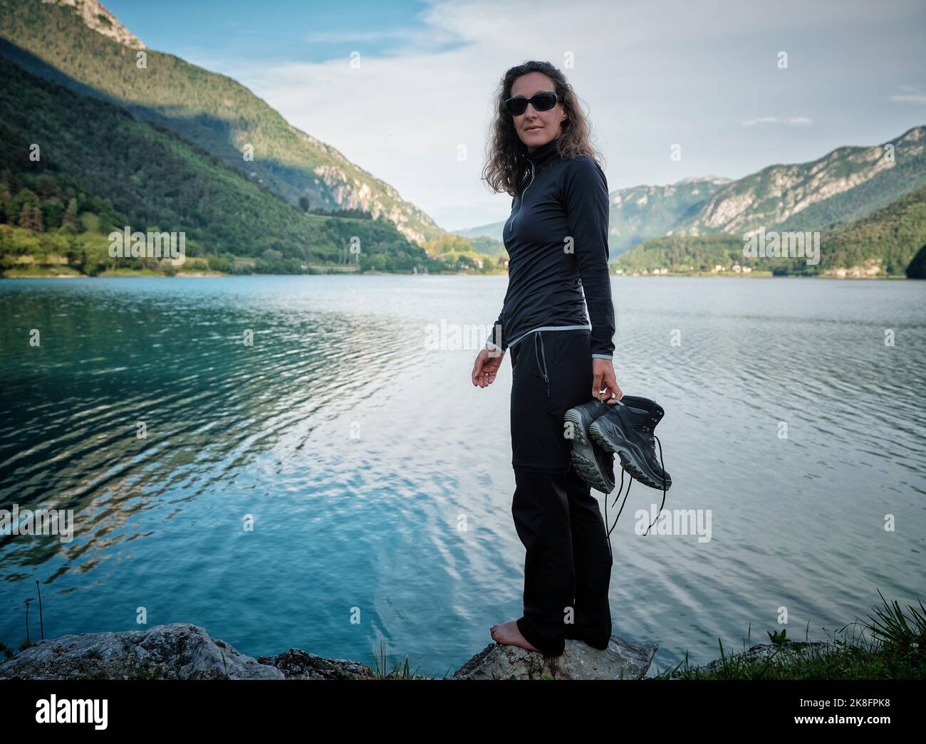 Femme souriante tenant des bottes debout sur le rocher au lac Banque D'Images