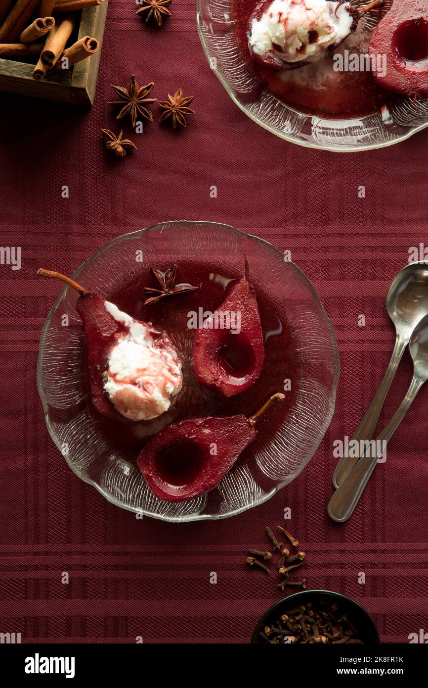 Portions de poires pochées épicées au vin rouge recouvertes de glace à la vanille. Banque D'Images