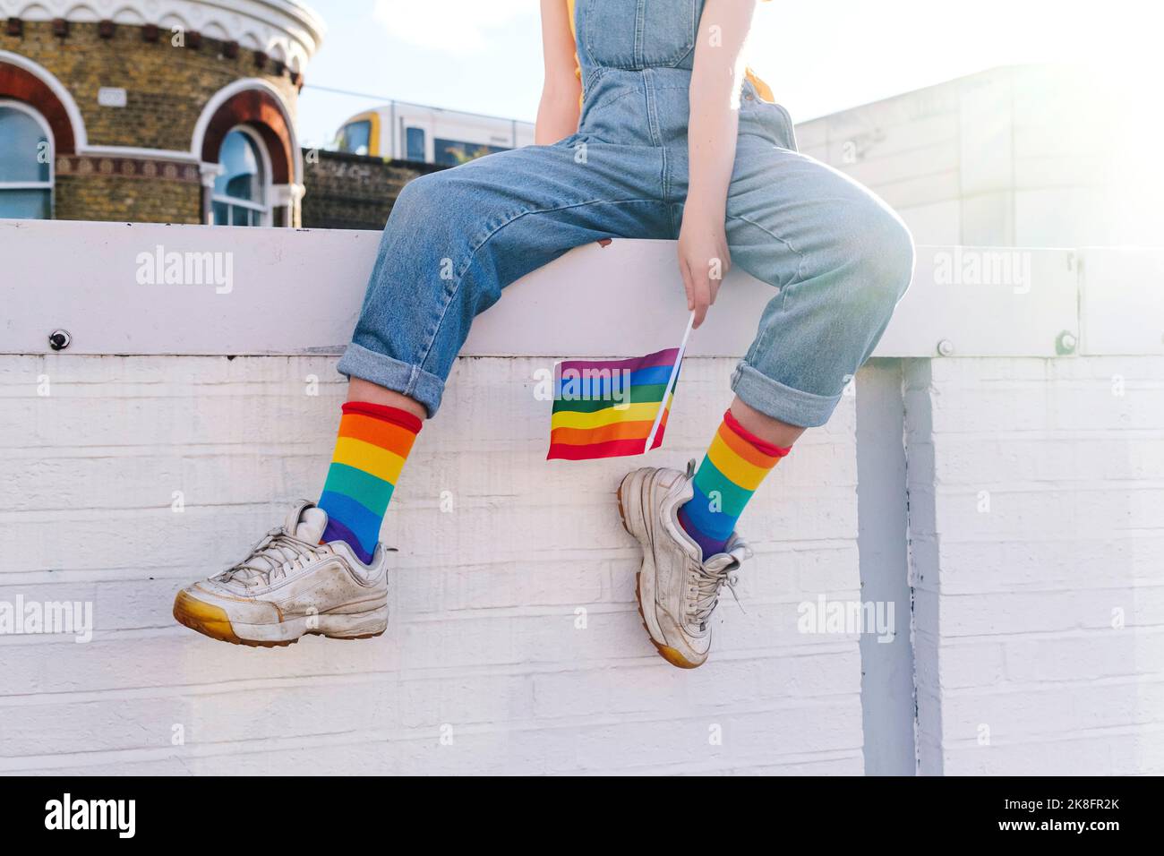 Personne transgenre avec drapeau arc-en-ciel assis sur le mur Banque D'Images