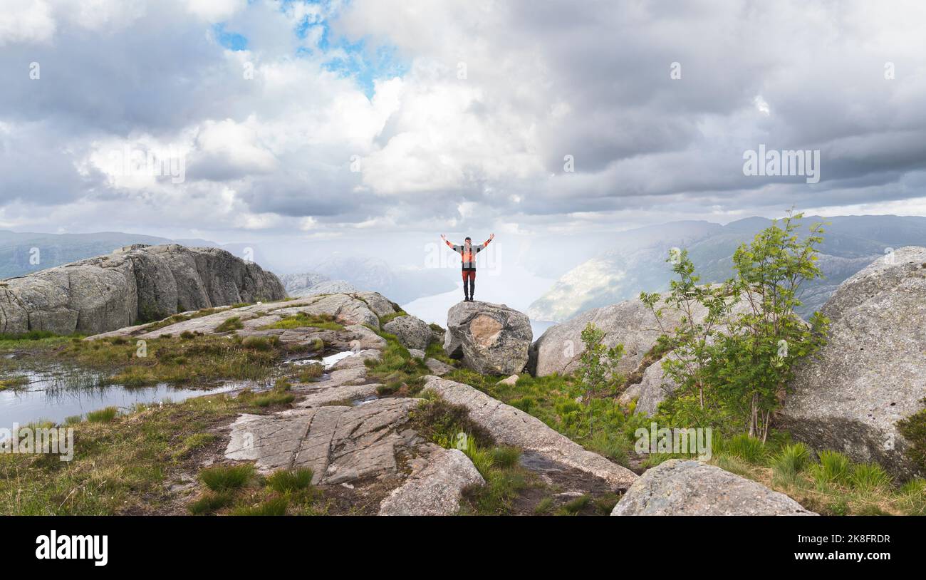Jeune randonneur aux bras levés sur la roche sous un ciel nuageux Banque D'Images