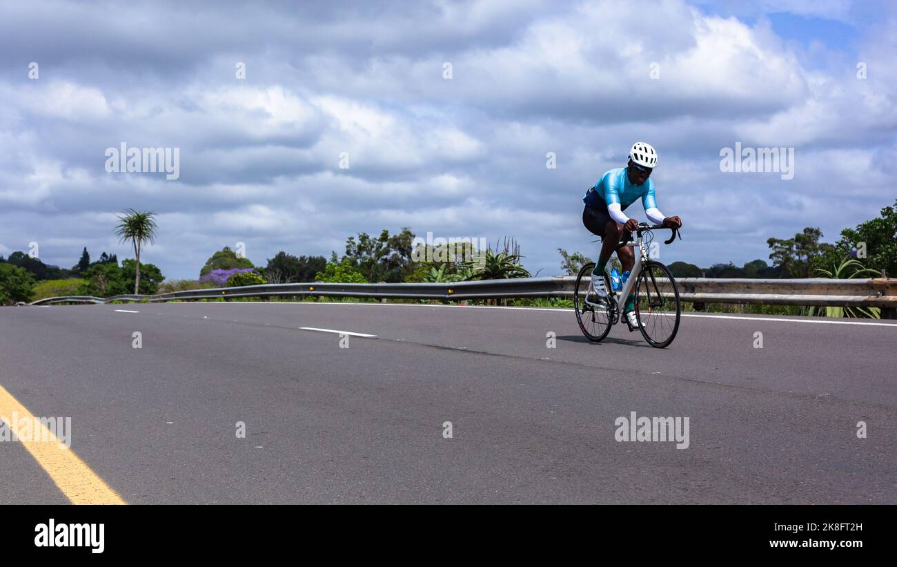 Cycliste athlète africain sur sa course de vélo solo dans la course sur la route ouverte. Banque D'Images