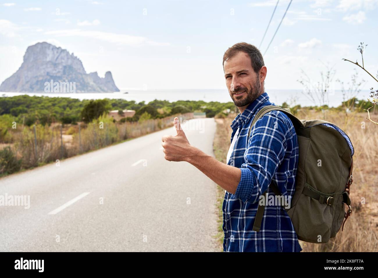 Homme souriant portant un sac à dos qui fait des gestes sur la route Banque D'Images