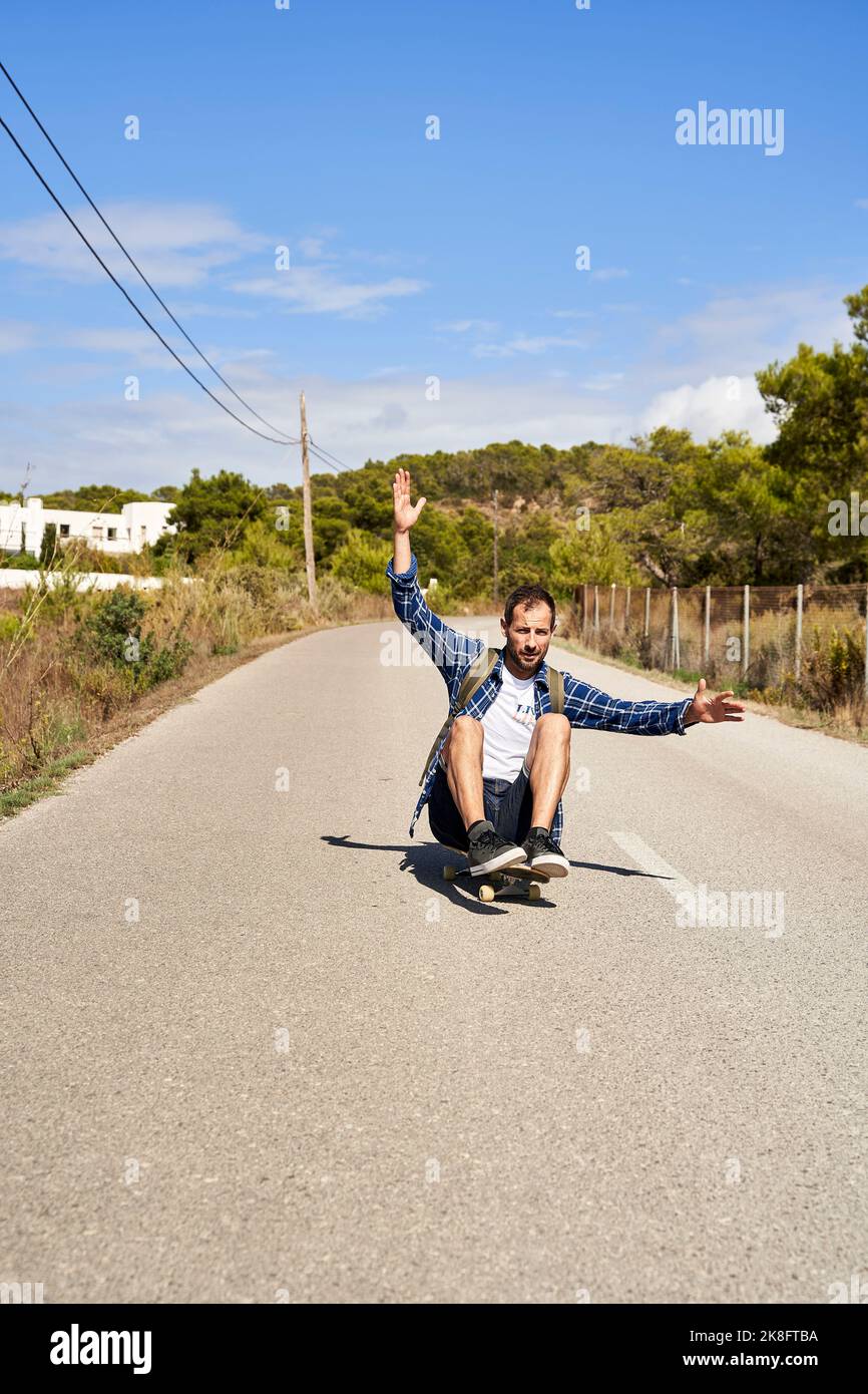 Homme levé à la main et faisant du skateboard sur la route Banque D'Images