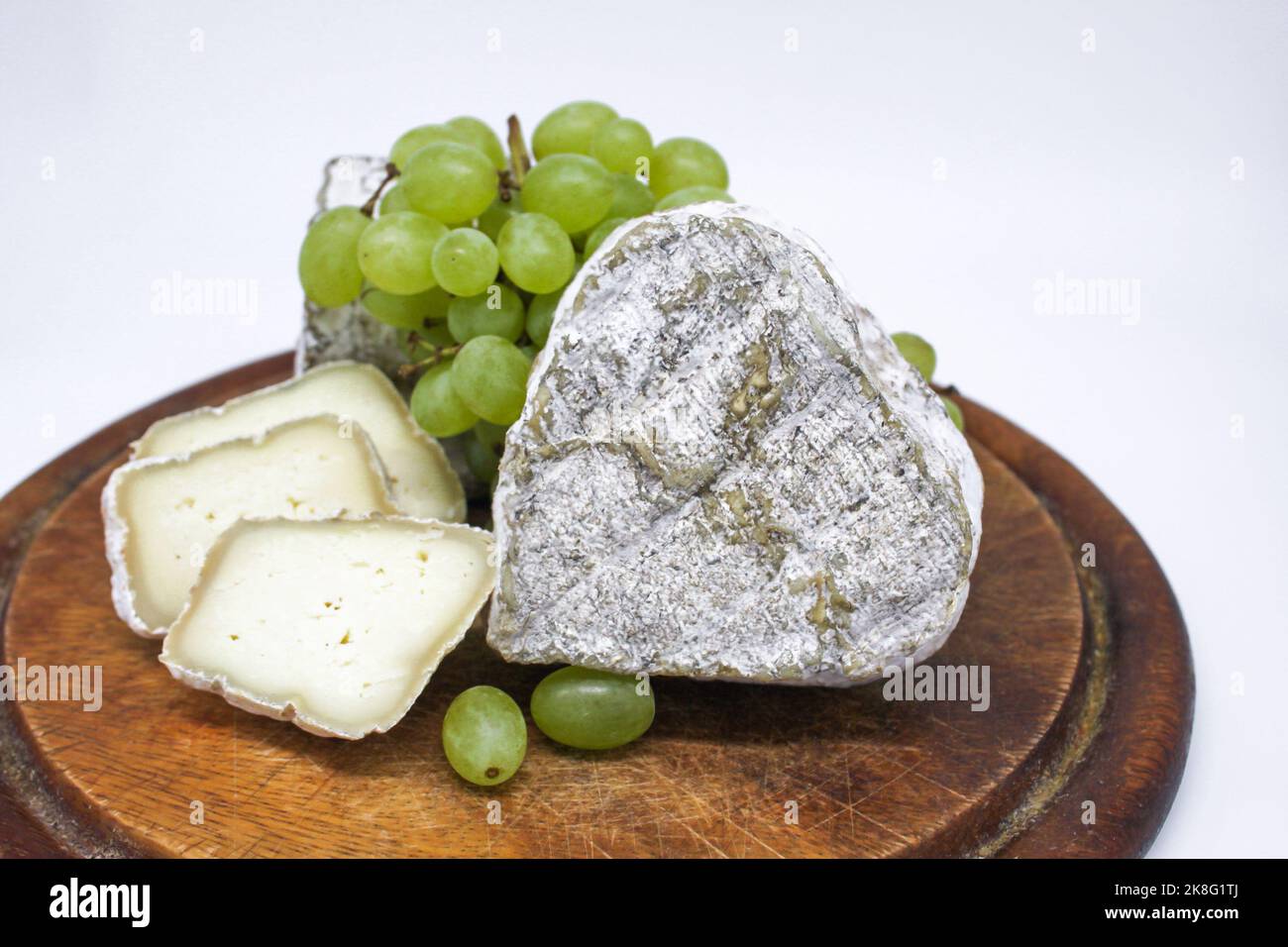 Assortiment de fromages bleu moldy lait de chèvre sur une planche à découper en bois avec des raisins verts. Arrière-plan blanc. Banque D'Images
