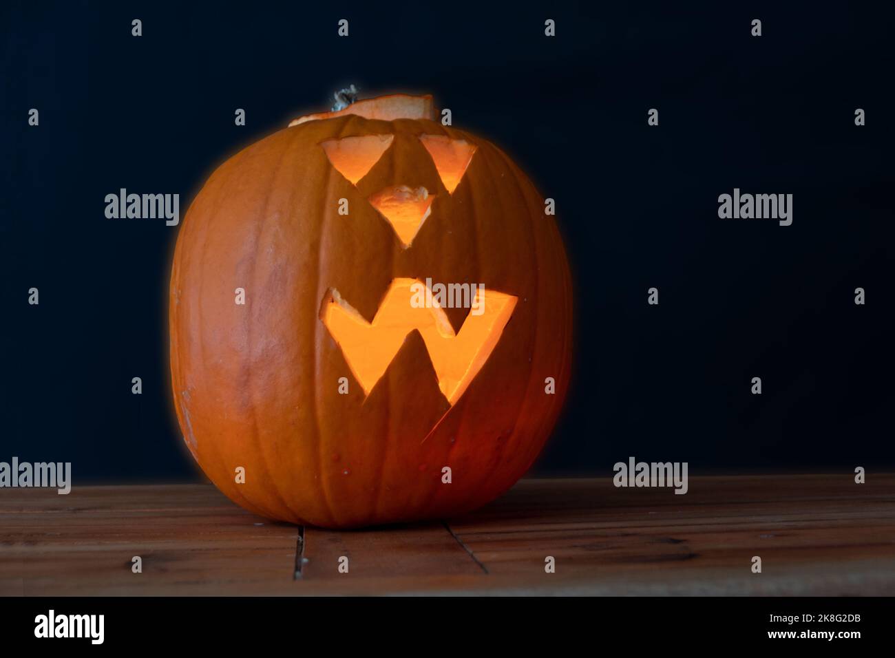 Grüsseliger Halloween Kürbis beleuchtet, auf Holztisch vor dunklem hintergrund Banque D'Images