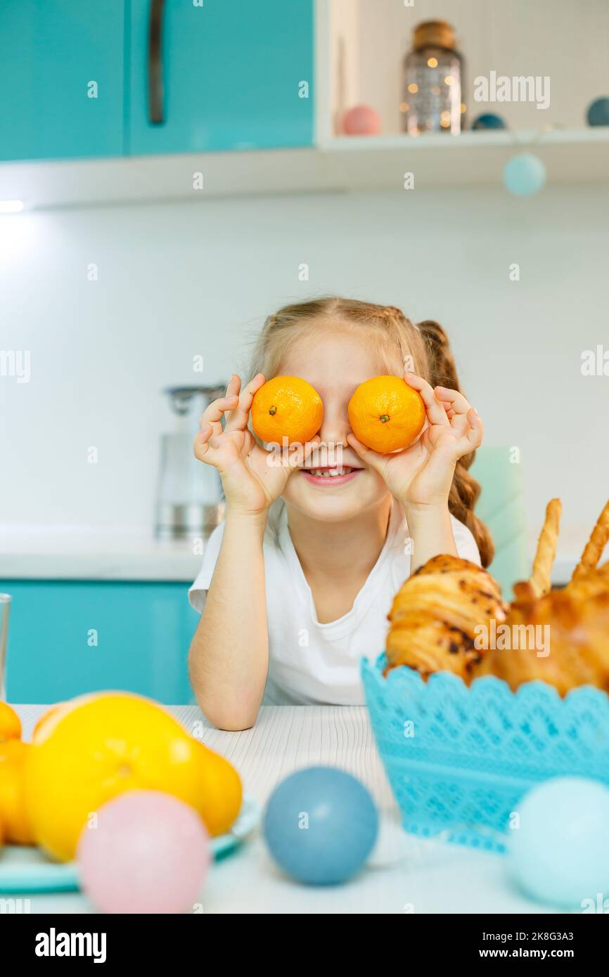 Une fille de 7-8 ans est assise dans la cuisine et fait des yeux avec une mandarine. Banque D'Images