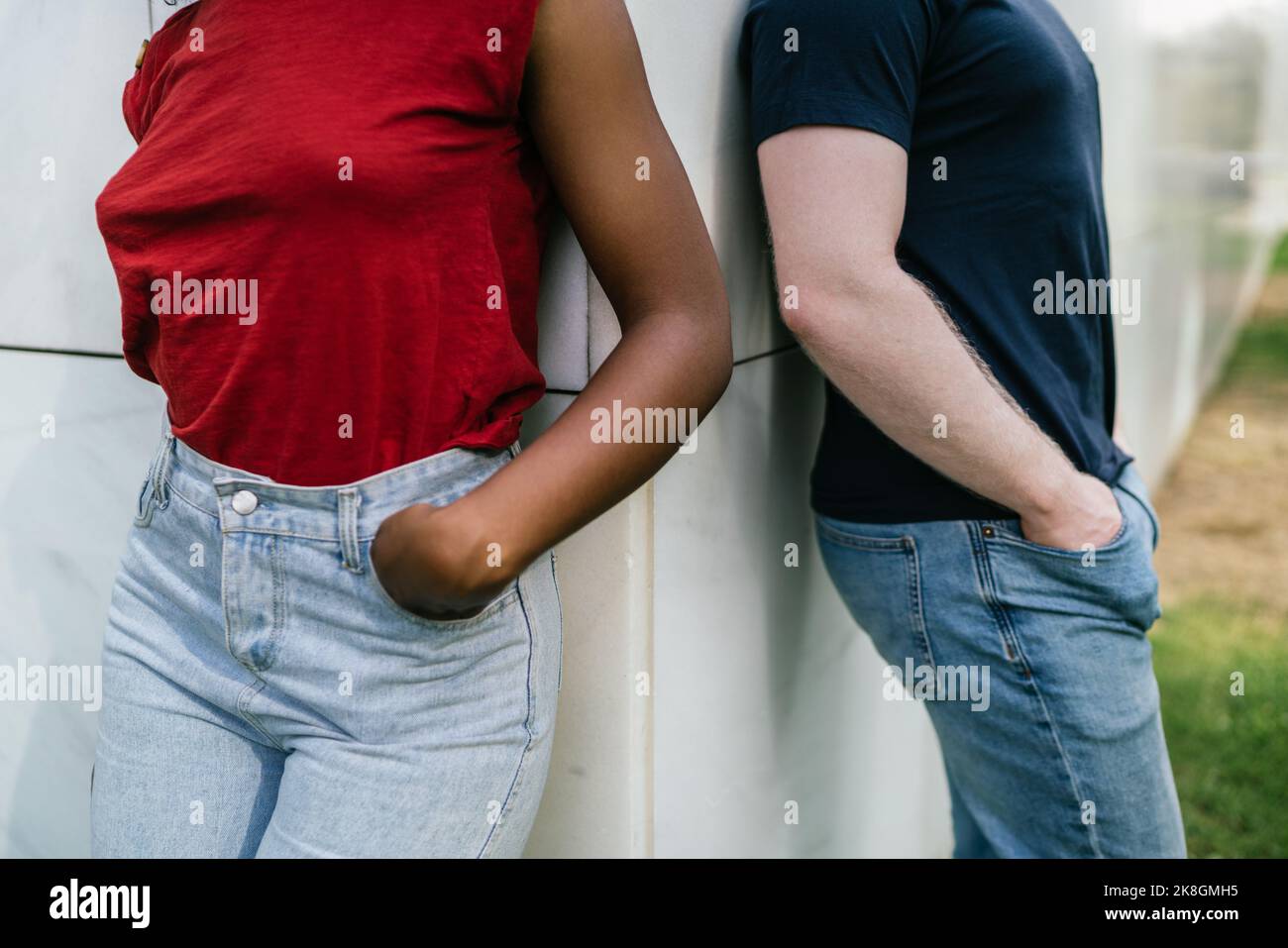 Cachez un petit ami et une petite amie multiracial méconnaissable en jeans et t-shirts inclinés sur un mur blanc avec les mains sur la poche Banque D'Images Cachez un petit ami et une petite amie multiracial méconnaissable en jeans et t-shirts inclinés sur un mur blanc avec les mains sur la poche Banque D'Images