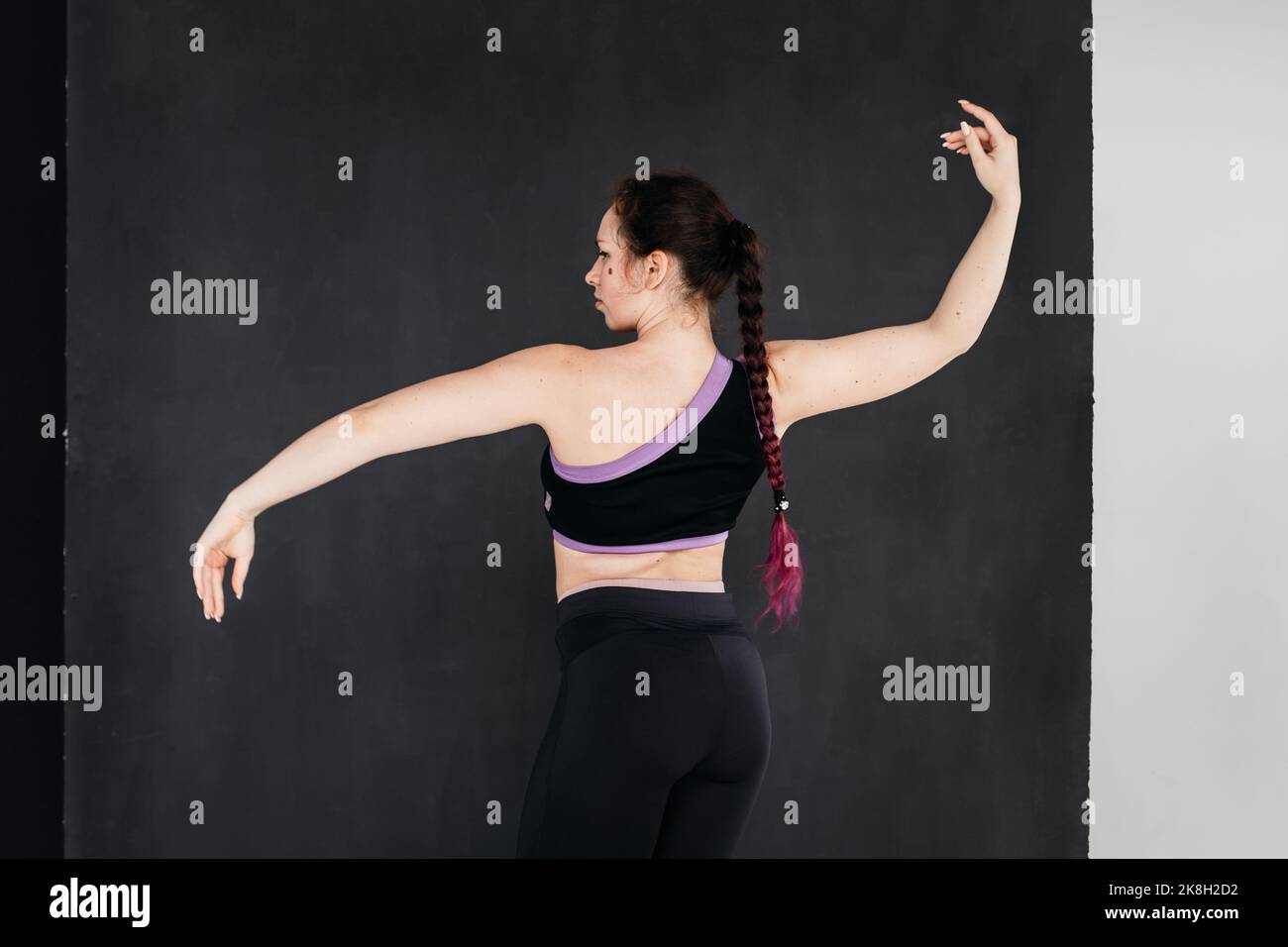 Une jolie fille brunette dansant. Arrière-plan foncé. Mouvements du corps fluides. Portrait studio d'une jeune femme sportive dans un pantalon et un haut noirs. Féminité co Banque D'Images