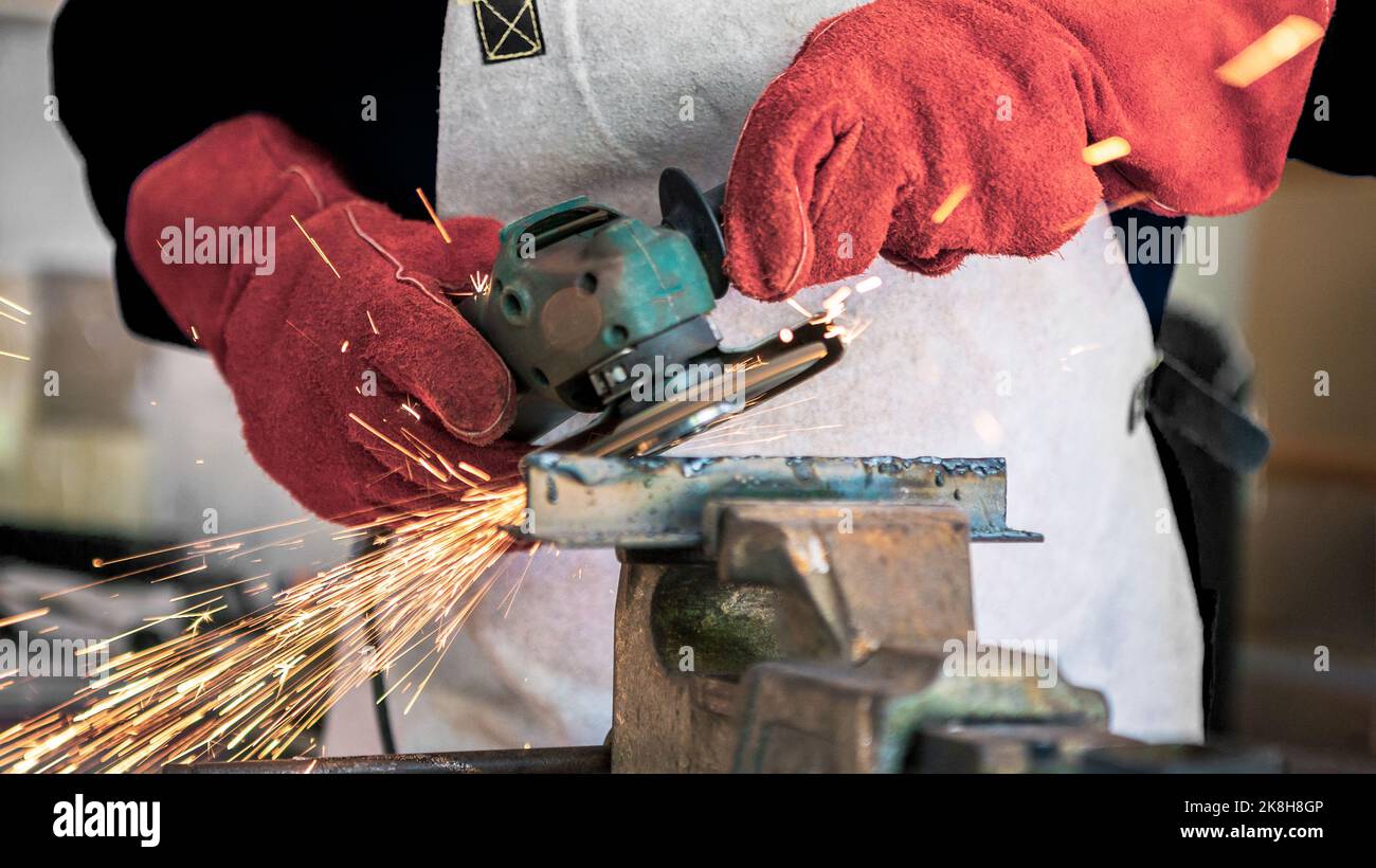Traitement du métal avec un homme utilisant une meuleuse d'angle pour nettoyer le joint en acier. Serrurier dans des vêtements et des gants spéciaux travaille en production. Étincelles en mét Banque D'Images