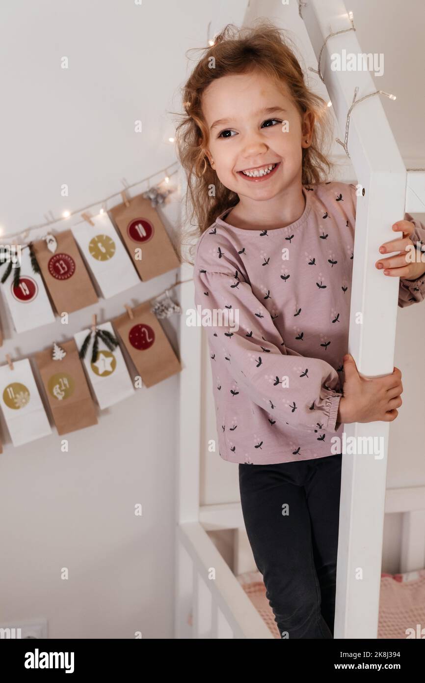 Un enfant en bas âge reçoit une nouvelle tâche du calendrier de l'AVENT, en attendant Noël.Ambiance festive pour une jolie petite fille au style curly.Enfant prend le sac de l'Avent avec les dates du mur à Banque D'Images