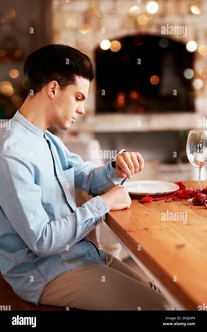 Je ne pense pas que des shes se présentent. Un homme qui vérifie l'heure tout en attendant sa date à une table de salle à manger. Banque D'Images