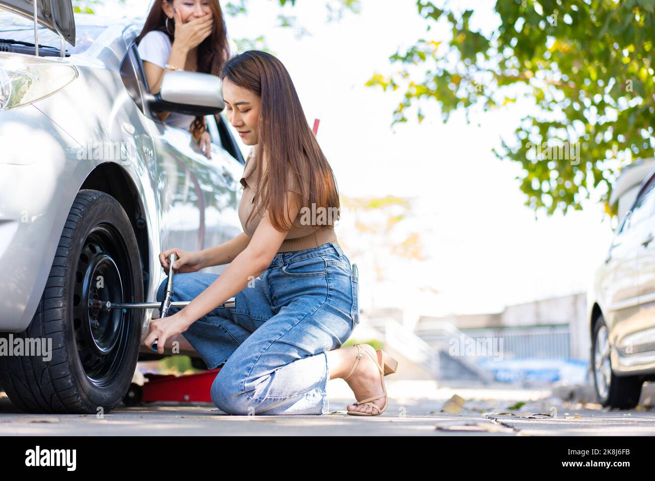 Une femme asiatique intelligente et attirante prend sa voiture et utilise  une clé pour changer la roue d'une voiture cassée, utilise des outils ou de  l'équipement, tente de résoudre la probl Photo