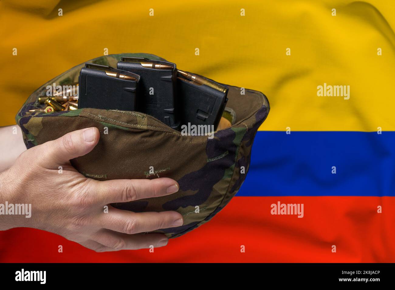 Un casque militaire avec cartouches et magazines pour un fusil dans les mains d'un homme sur le fond du drapeau de la Colombie. Le concept de Banque D'Images