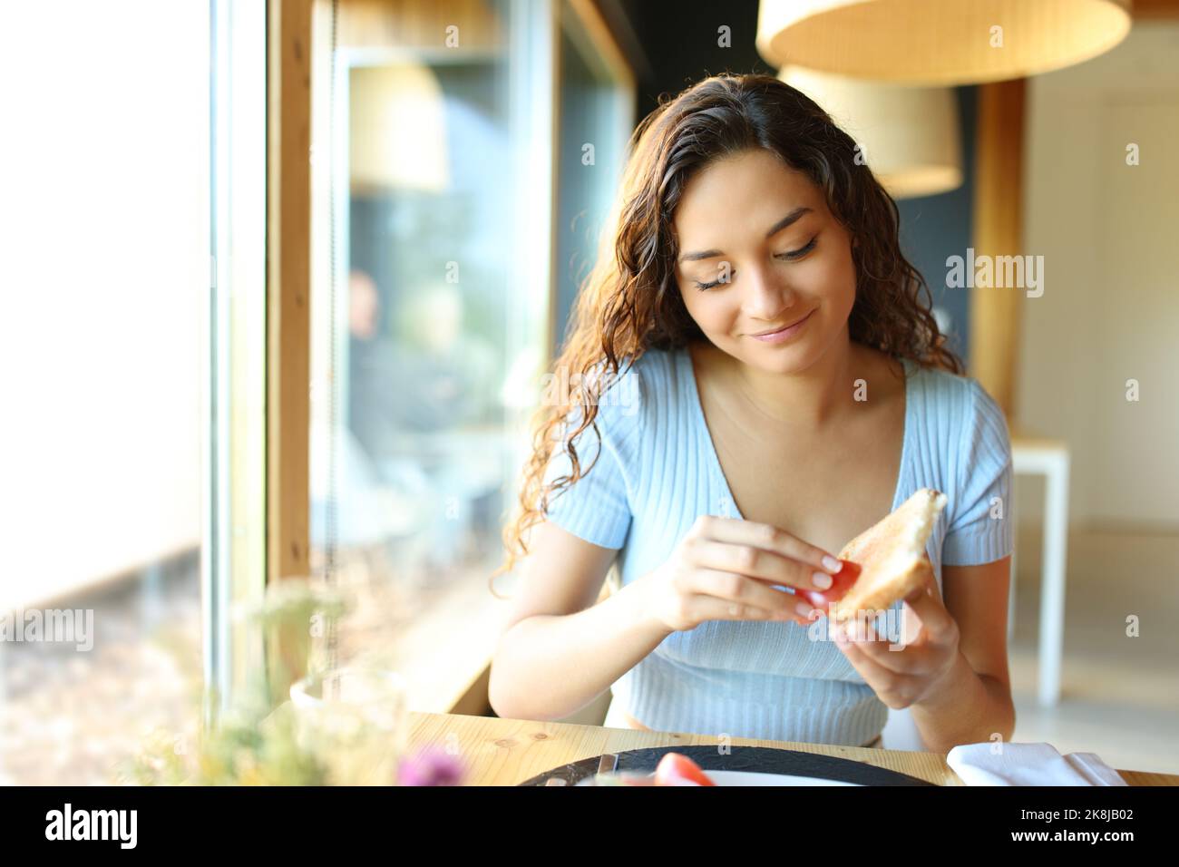Vue de face d'une femme heureuse qui répandait de la tomate sur du pain assis dans un restaurant Banque D'Images