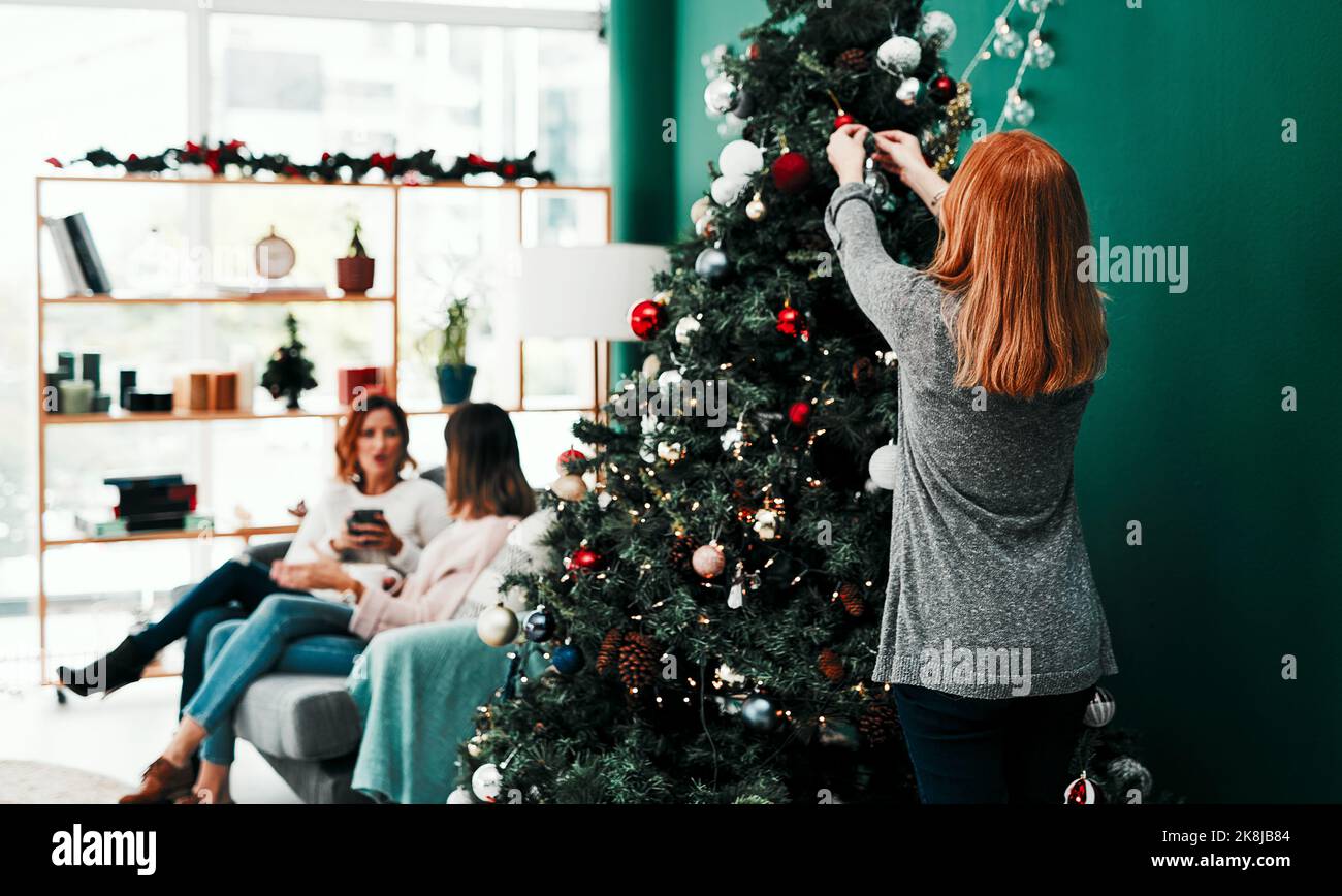Aider avec un peu de décorations. Photo d'une femme méconnaissable décorant un arbre de Noël à la maison pendant la journée. Banque D'Images