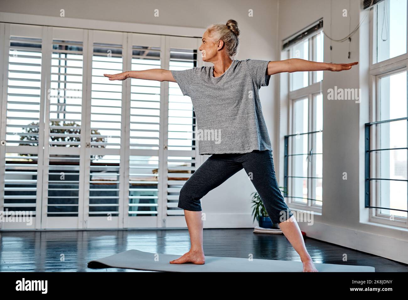 Regardez la vue à l'extérieur. Une femme mature et détendue pratiquant le yoga dans un studio pendant la journée. Banque D'Images