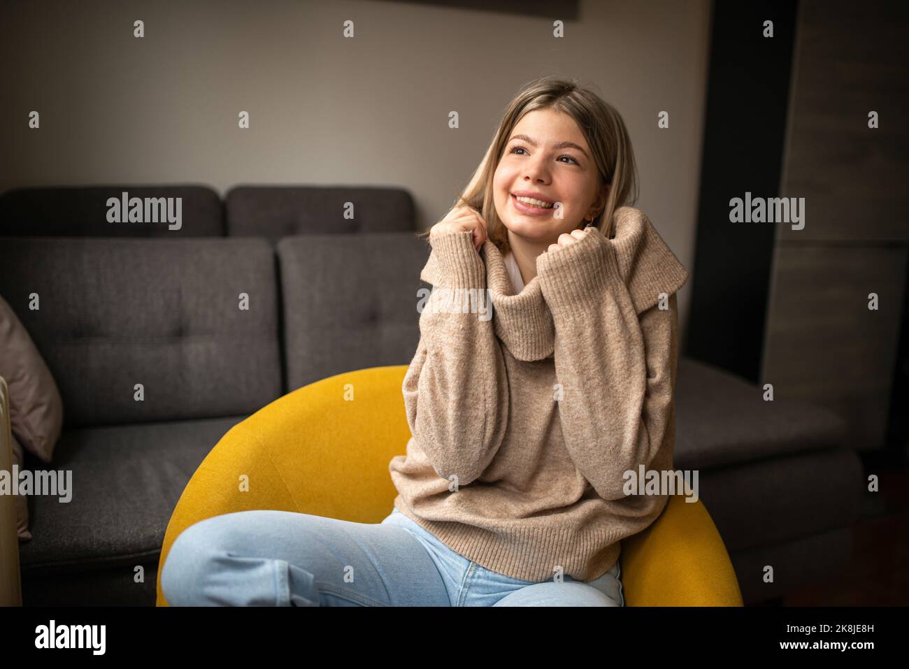 Bonne jeune femme assise sur un canapé à la maison. Portrait de femme confortable en vêtements d'hiver reposant sur un fauteuil. Portrait de belle fille souriant un Banque D'Images