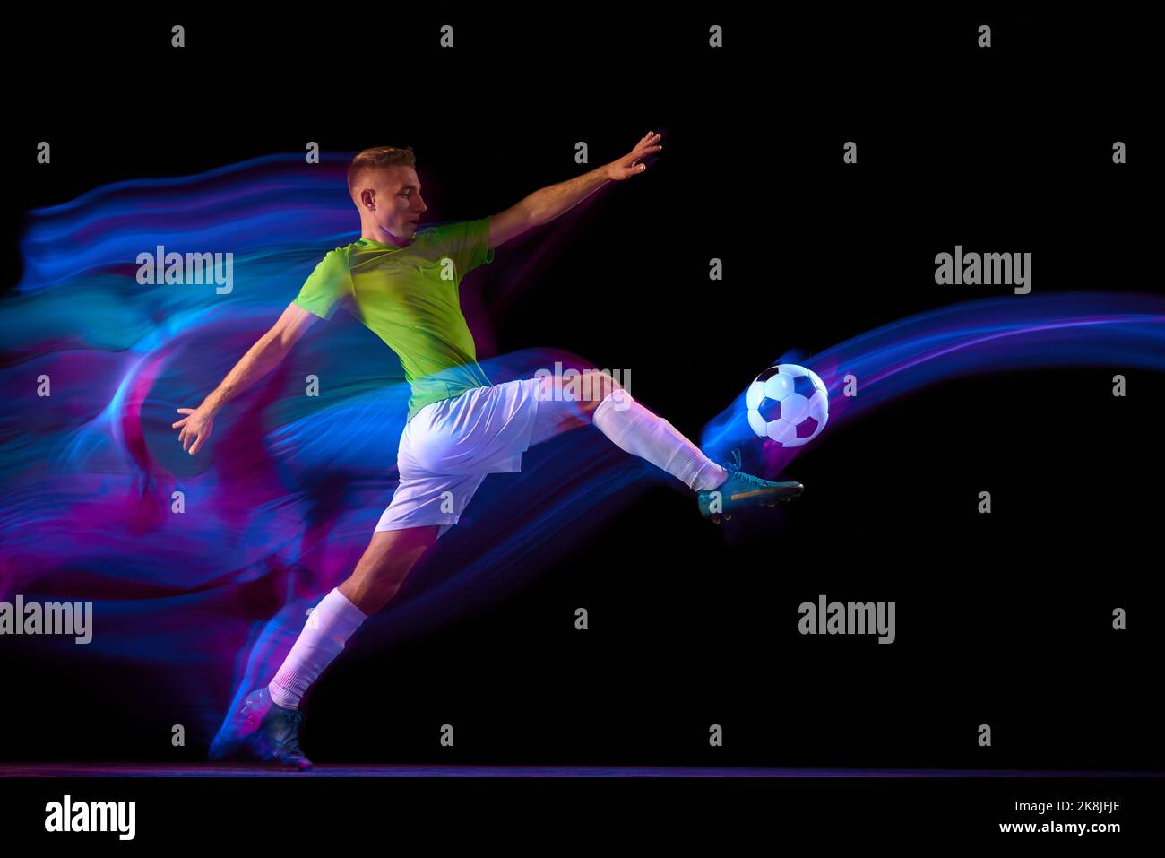 Le sport en action. Un joueur de football professionnel s'entraîne avec une  balle de football isolée sur fond sombre dans un filtre de lumière néon.  Sport, vitesse, puissance Photo Stock - Alamy