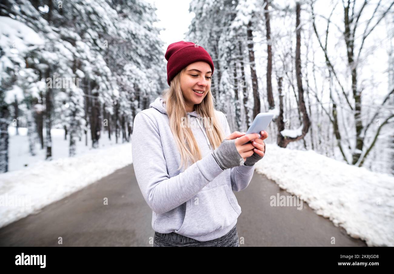 Sportswoman debout dans la nature à la neige hiver jour et SMS. Fitness en hiver, télécommunications, fitness en plein air Banque D'Images