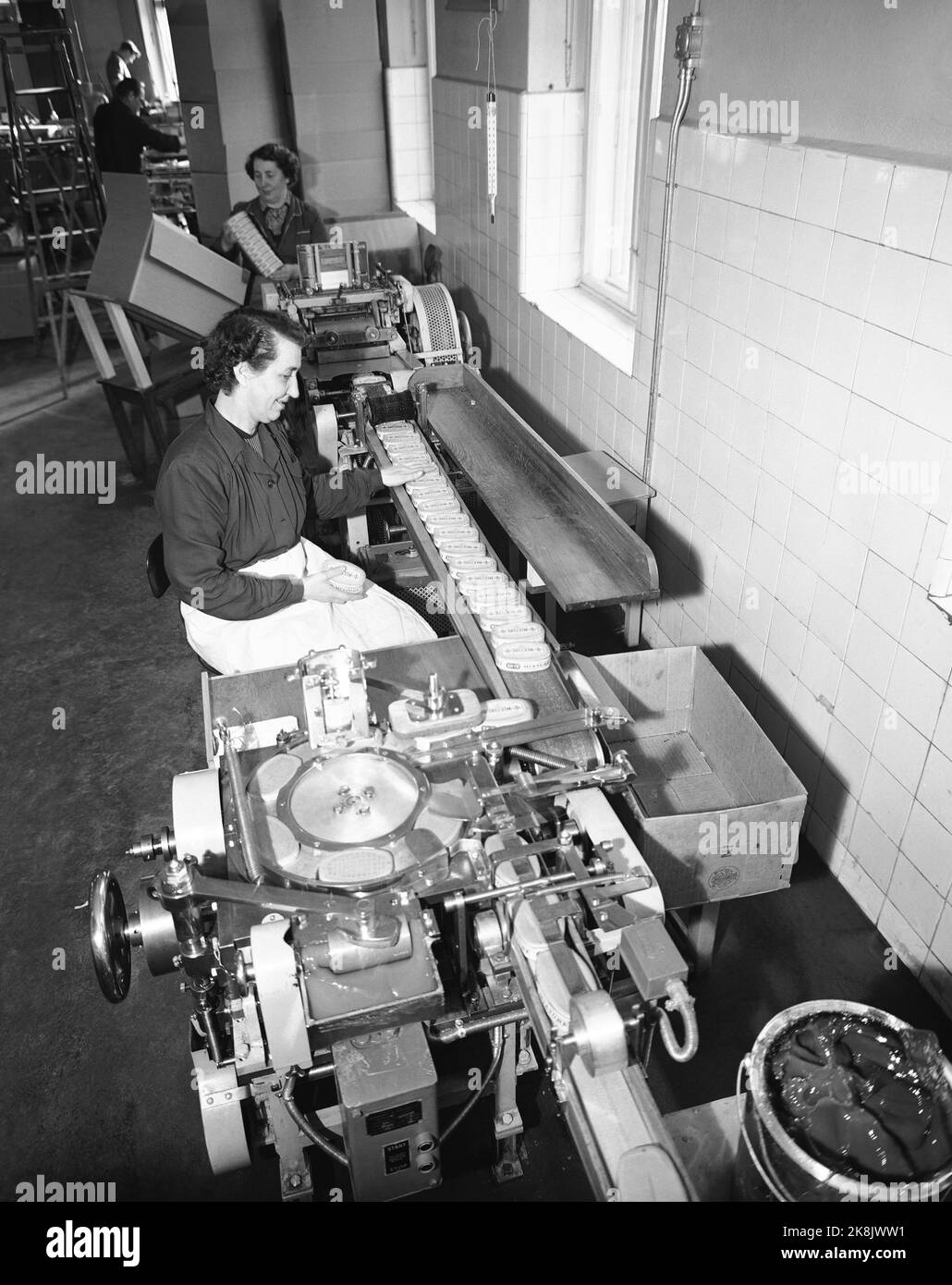 19550305 - usine de tabac de J. L. Tiedemann. Le processus final dans la section Pipetobac. Les cases remplies apparaissent sur les liens de fonctionnement et, dans les machines, sont appliquées des étiquettes supérieures et latérales ainsi que des marques de marquage. La femme vérifie que tout va bien. Photo: Aage Storløkken / actuel / NTB Banque D'Images