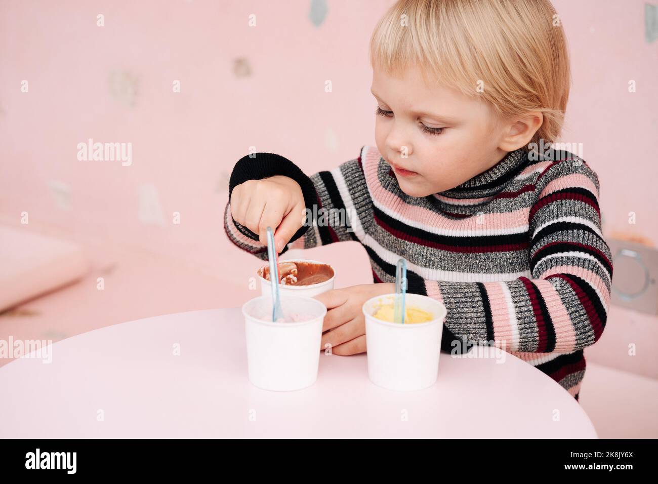 Un enfant mange de la glace dans un café. Ensemble de bols avec différentes crèmes glacées aux saveurs différentes et ingrédients frais Banque D'Images