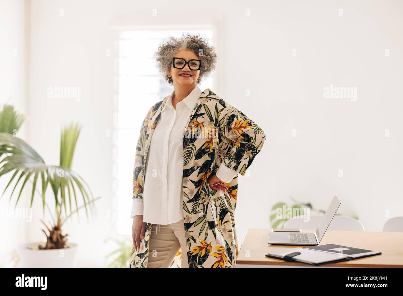 Femme d'affaires senior souriant à la caméra tout en se tenant à côté d'une table de conférence dans une salle de réunion. Bonne femme d'affaires attendant une réunion en un mois Banque D'Images