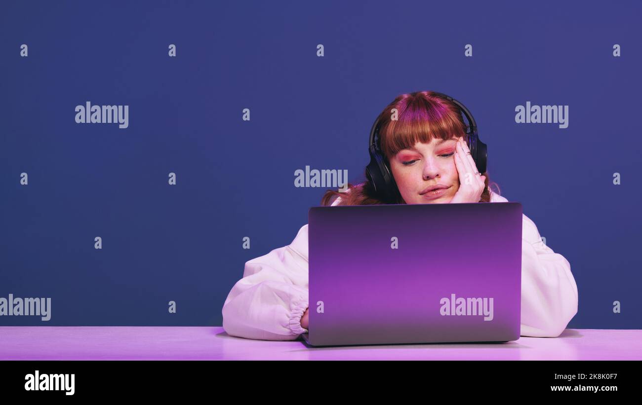 Femme aux cheveux de gingembre regardant son ordinateur portable de jeu soigneusement dans un studio. Jeune joueuse féminine utilisant un service de streaming interactif pendant qu'elle est assise Banque D'Images