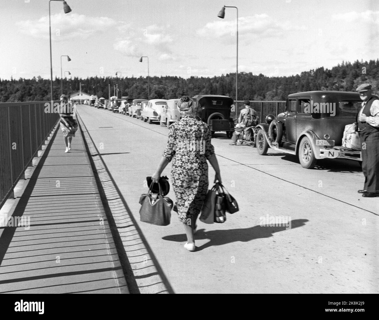 Svinesund 1952 ; fièvre du sucre ! Les Norvégiens n'ont jamais traversé la crique pour de l'eau, mais souvent au-dessus de la quille pour d'autres marchandises. Dans la période d'après-guerre, le sucre était un bien attendu depuis longtemps, car il était rationné jusqu'en 1952. Lorsqu'il a été autorisé à importer 10 kilos de sucre par voyageur, le commerce frontalier a explosé. Les automobilistes norvégiens ont rempli la voiture de '' sucrier les enfants '' qui valait leur poids dans, sinon l'or, donc au moins dans le sucre! Cette femme de ménage porte les sacs pleins et la robe florale typique. Photo; Sverre A. Børretzen / actuel / NTB Banque D'Images