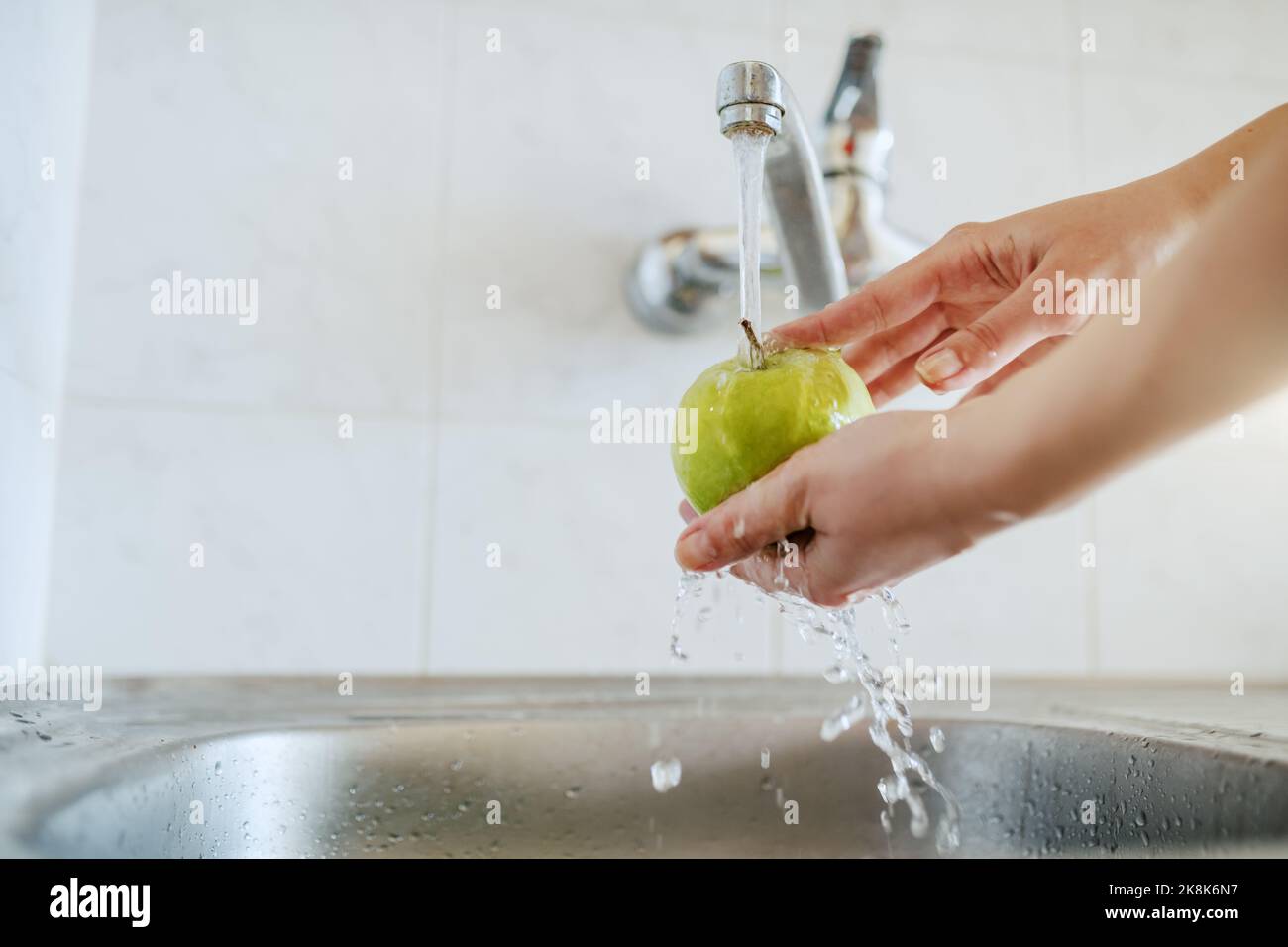 Gros plan de la femme caucasienne lavant la pomme verte dans l'évier. Banque D'Images